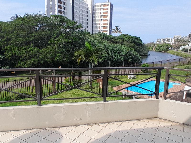 Spacious balcony featuring tiled flooring and a metal balustrade, offering elevated views of the complex garden, swimming pool, and surrounding landscape.