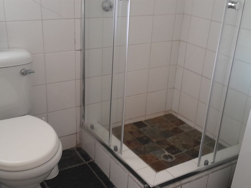 A functional bathroom featuring a shower enclosure, toilet, and vanity basin with tiled finishes. The space shows signs of wear and requires minor maintenance.