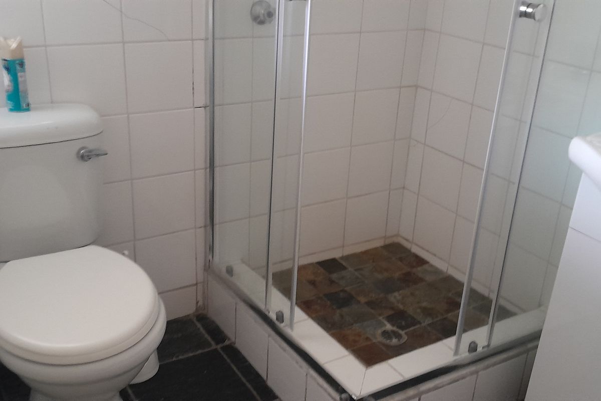 A functional bathroom featuring a shower enclosure, toilet, and vanity basin with tiled finishes. The space shows signs of wear and requires minor maintenance.