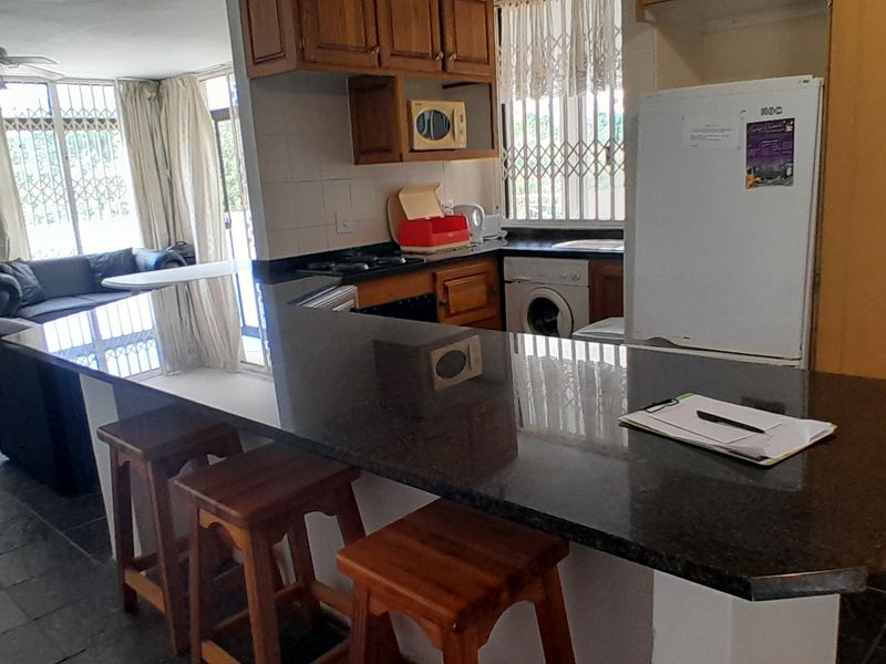 Open-plan living and kitchen area featuring a granite breakfast bar, built-in wooden cabinetry, and tiled flooring throughout.