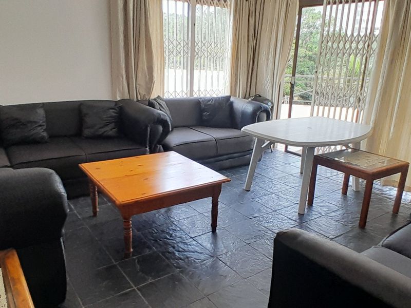 A living room featuring dark tiled flooring, large windows with security gates, and access to an outdoor area through a sliding glass door.