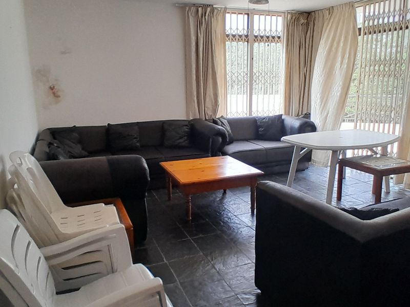 A living room area featuring dark tiled flooring and access to an outdoor space through a security gate and sliding door.
