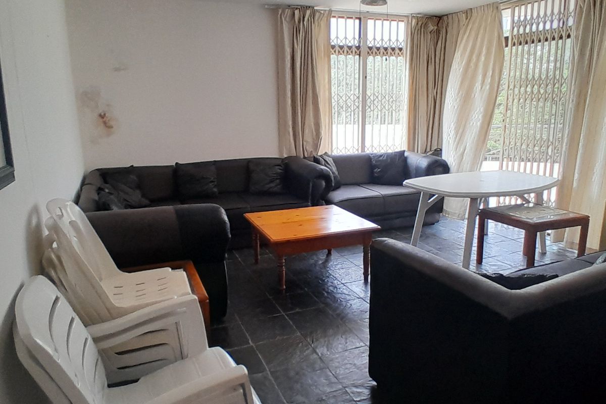A living room area featuring dark tiled flooring and access to an outdoor space through a security gate and sliding door.