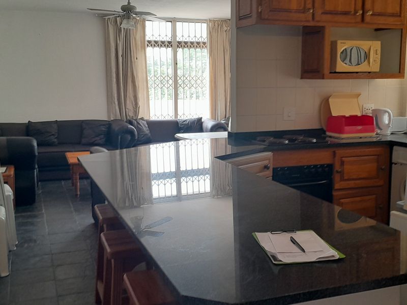 Open-plan living and kitchen area featuring a granite breakfast bar, wooden cabinetry, and tiled flooring, with visible wall damage requiring repair.