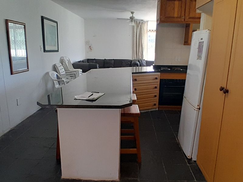 Open-plan living and kitchen area featuring a central island, built-in cabinetry, and dark tiled flooring, offering a functional layout with potential for modernization.