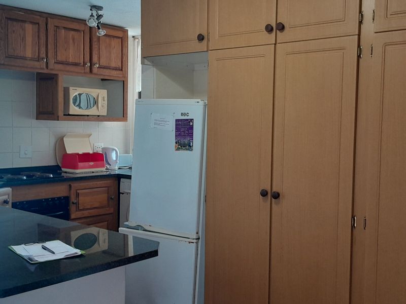 A functional kitchen featuring wooden cabinetry, dark stone countertops, and a tiled backsplash, with an open-plan layout connecting to the living area.