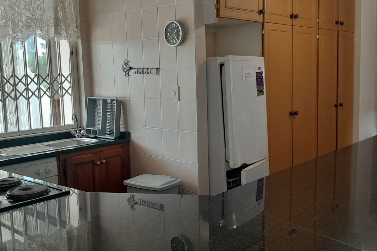 A functional kitchen featuring granite countertops, ample built-in cabinetry, a stainless steel sink, and an integrated electric hob with a tiled backsplash.