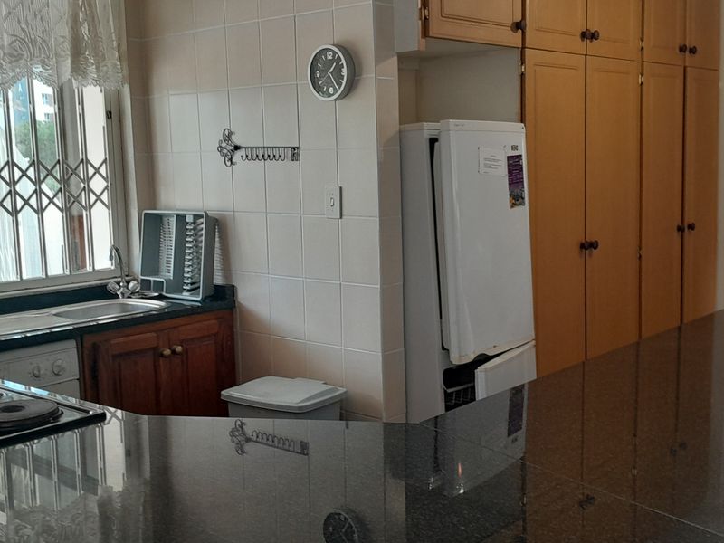 A functional kitchen featuring granite countertops, ample built-in cabinetry, a stainless steel sink, and an integrated electric hob with a tiled backsplash.