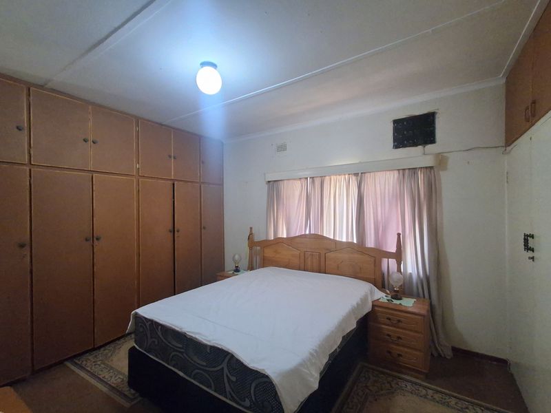 A bedroom featuring extensive built-in wooden cupboards, a central ceiling light, and a window with curtain rails.