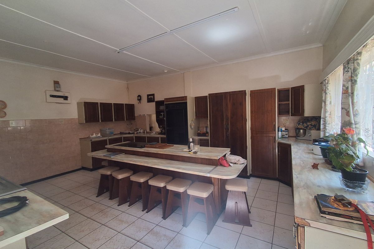 Spacious kitchen featuring extensive built-in wooden cabinetry, a central island with integrated seating, and tiled flooring, offering significant potential for modern renovation.