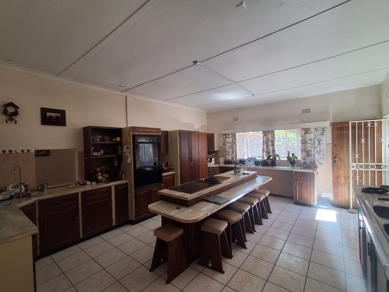 Spacious kitchen featuring a central island with integrated hob, ample built-in cabinetry, and tiled flooring, offering a functional layout with potential for modernization.