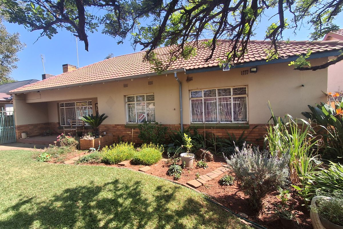 A view of the rear facade featuring a tiled roof, brick base, steel-framed windows with security bars, and a well-maintained garden area.