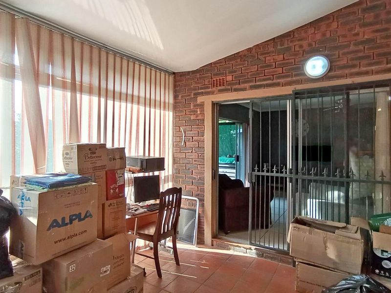 A covered patio area featuring exposed brick walls, terracotta flooring, and large windows, providing a versatile space for indoor-outdoor living.