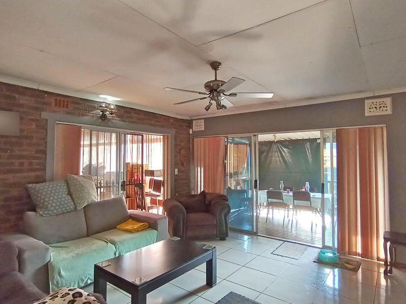 Spacious living room featuring tiled flooring, an exposed brick feature wall, and large sliding glass doors providing access to the outdoor patio area.
