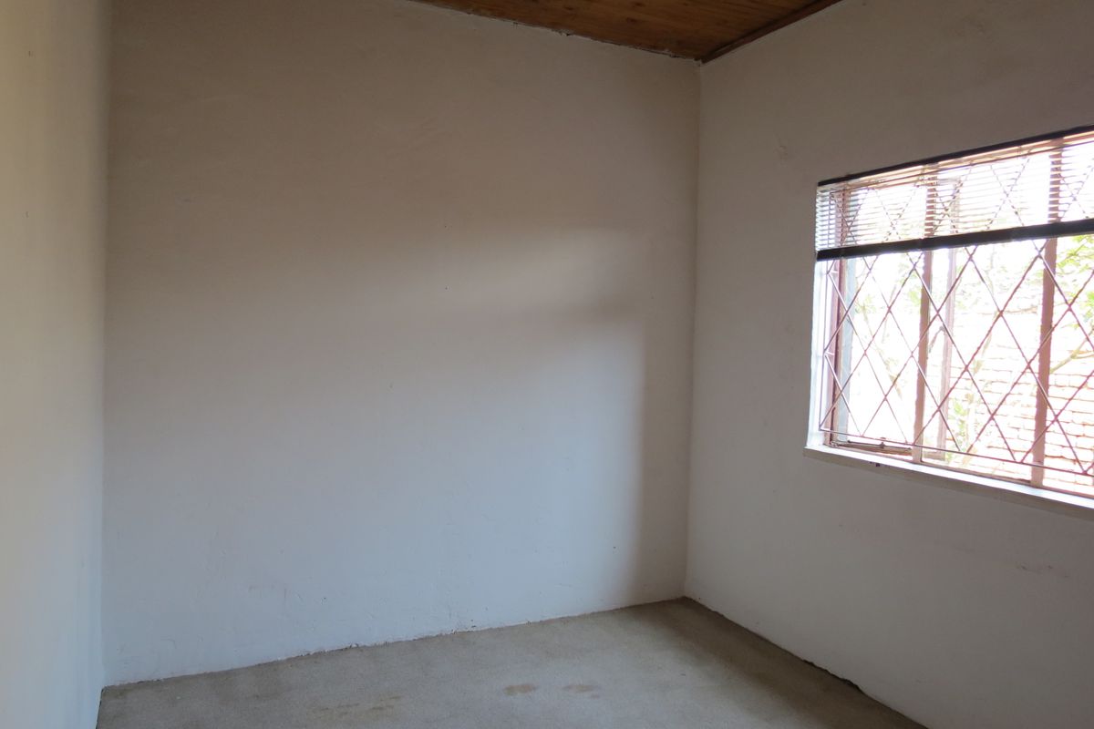 An empty bedroom featuring a timber ceiling, a window with a security gate, and plain wall finishes, offering a blank canvas for renovation.