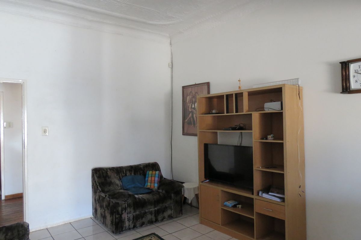 A living room featuring tiled flooring and decorative pressed metal ceilings, requiring some cosmetic updates to the walls and electrical finishes.