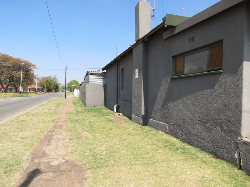 Side view of the property showing the exterior plastered wall, chimney, and metal roofing along the street-facing boundary.