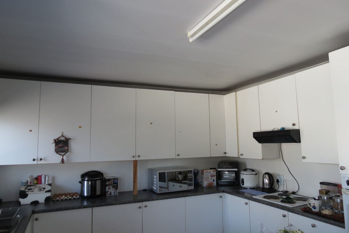 A functional kitchen featuring white cabinetry, dark laminate countertops, and an integrated extractor fan, requiring minor cosmetic updates to improve its overall aesthetic appeal.