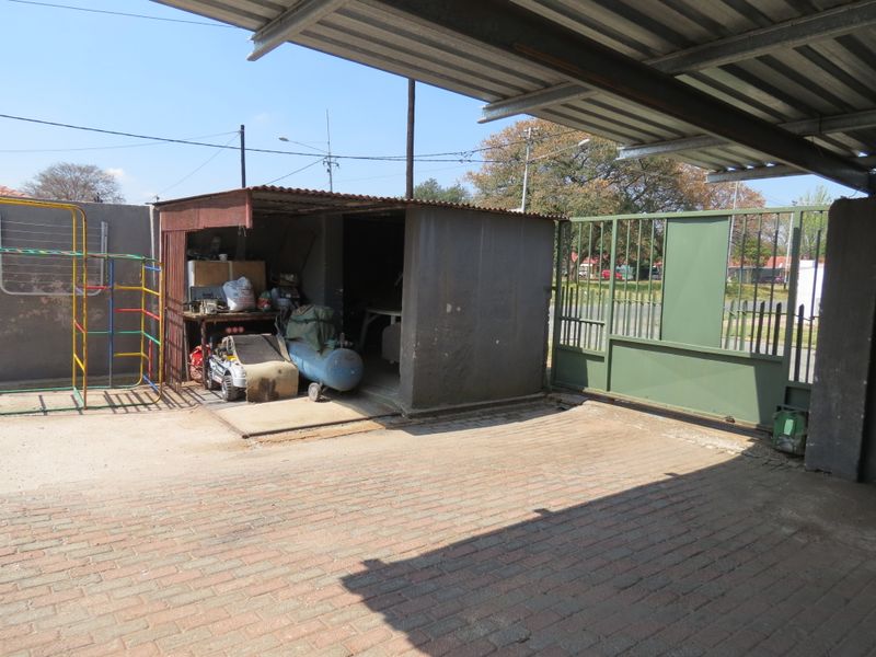 Outdoor area featuring a paved driveway, sliding metal gate, and a corrugated metal storage shed structure.
