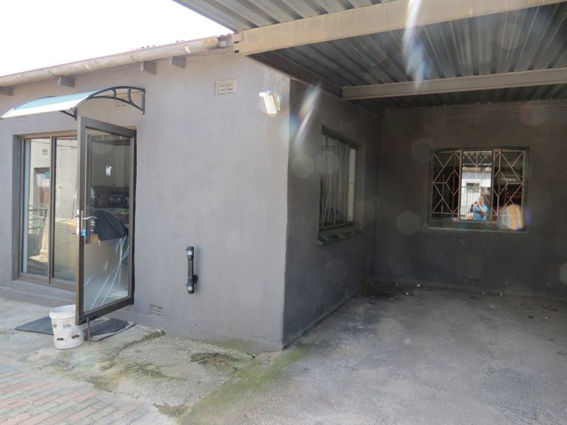 Rear exterior view showing a covered parking area, paved flooring, and a sliding glass door with visible damage.