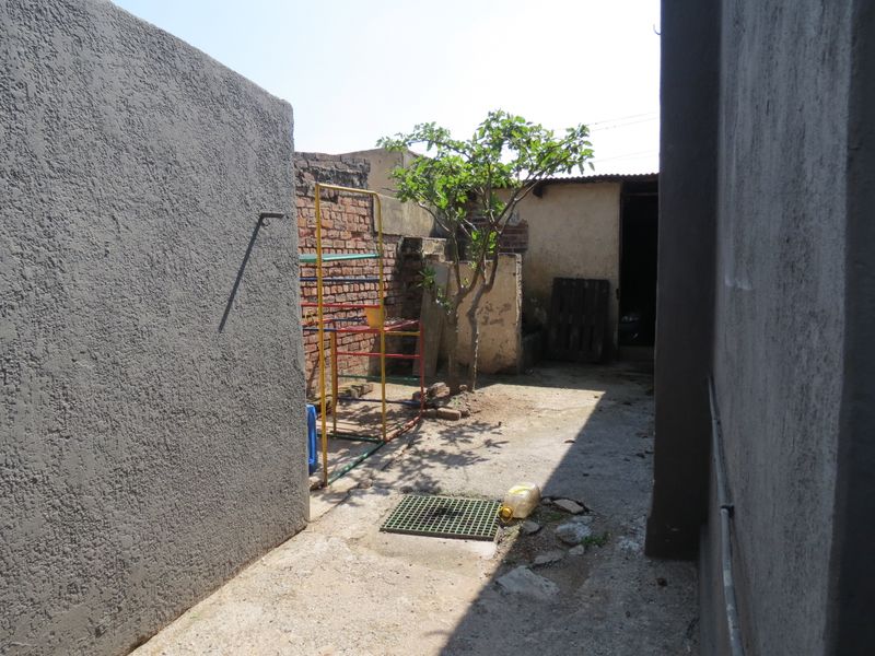 A narrow rear exterior area featuring concrete paving, a brick boundary wall, and a drainage point, requiring maintenance and landscaping improvements.