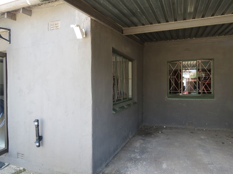 A covered outdoor patio area featuring a corrugated metal roof, concrete flooring, and security bars on the windows.