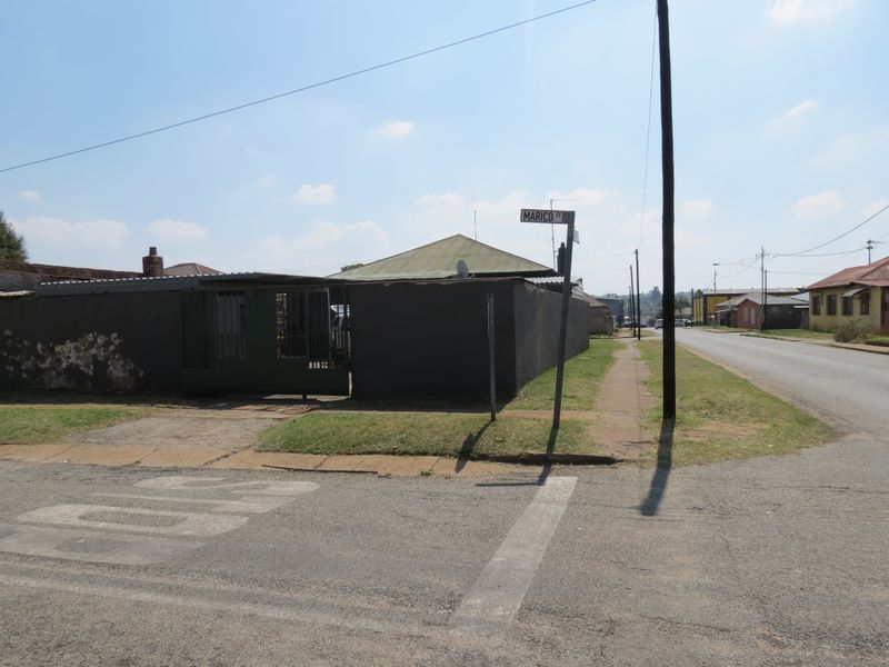 Street view of the property corner showing the perimeter wall, metal gate, and roof structure from the road intersection.