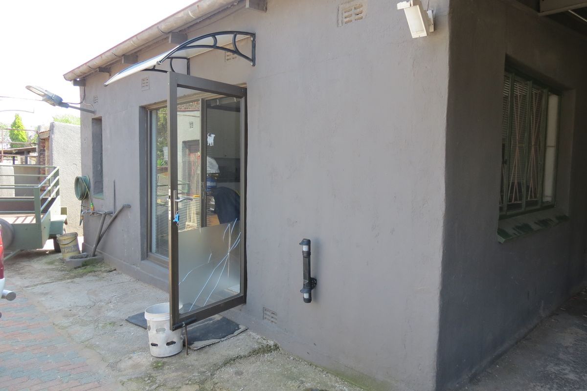 Rear exterior view of the property featuring a paved area, an aluminium door with a canopy, and security window bars.