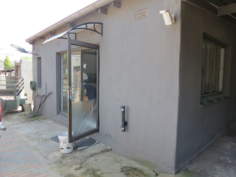 Rear exterior view of the property featuring a paved area, an aluminium door with a canopy, and security window bars.