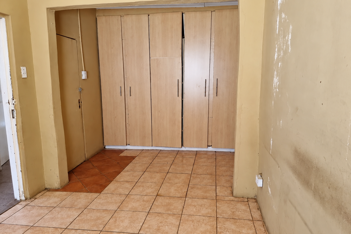 An empty bedroom featuring built-in wooden cupboards and tiled flooring, requiring cosmetic attention to the wall finishes.