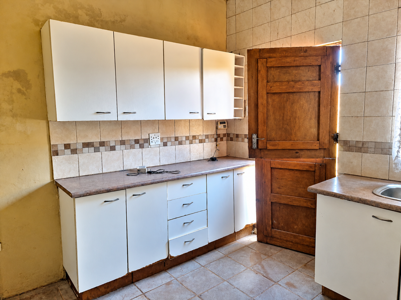 A dated kitchen featuring white cabinetry, laminate countertops, and tiled finishes, requiring cosmetic updates and repairs to the wall surfaces and cabinet bases.