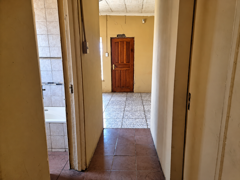 A view through a hallway connecting to a bathroom and another room, featuring tiled flooring and visible wall damage requiring maintenance.