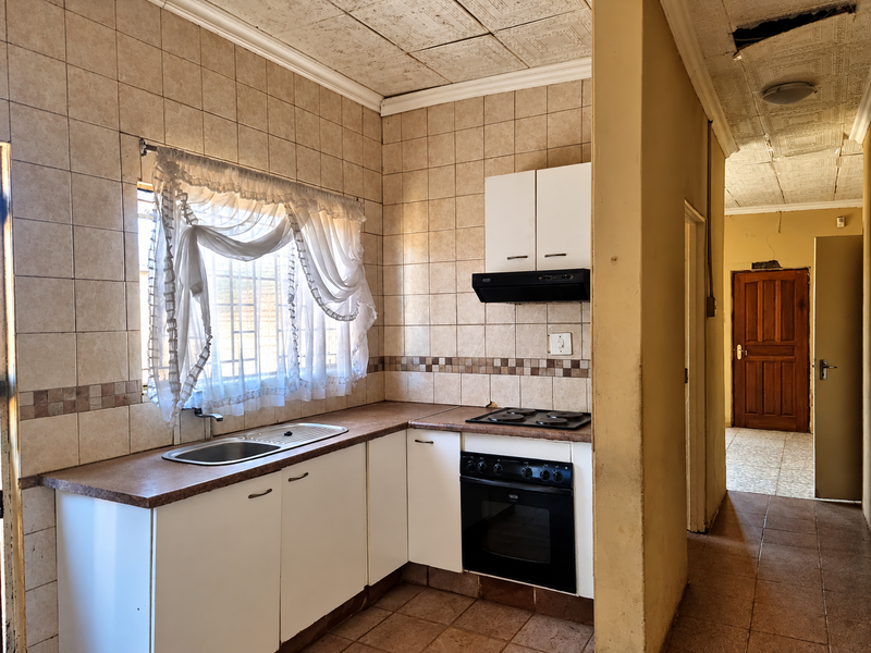A dated kitchen featuring built-in cabinetry, an integrated oven and hob, and tiled finishes, requiring cosmetic updates to modernize the space.