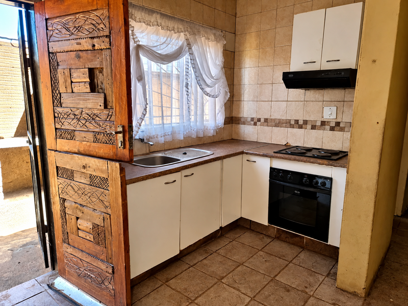 Compact kitchen featuring built-in cabinetry, integrated oven and hob, tiled backsplash, and direct access to an outdoor area via a decorative wooden security door.