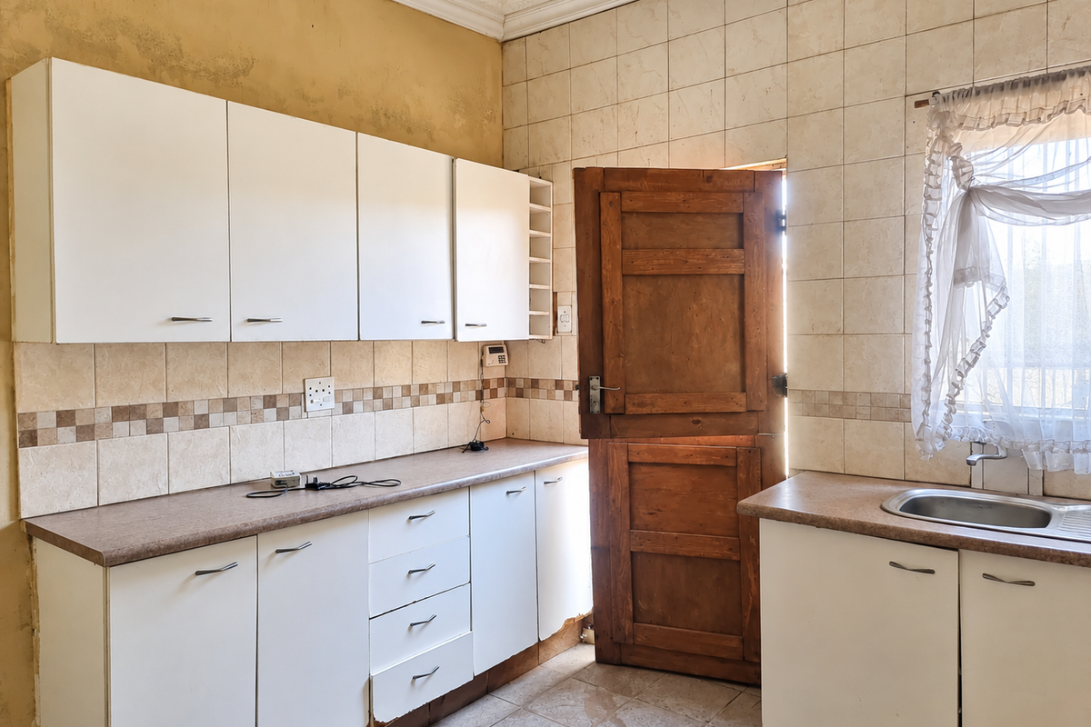 A dated kitchen featuring white cabinetry, tiled backsplash, and a stainless steel sink, requiring cosmetic updates to modernize the space.