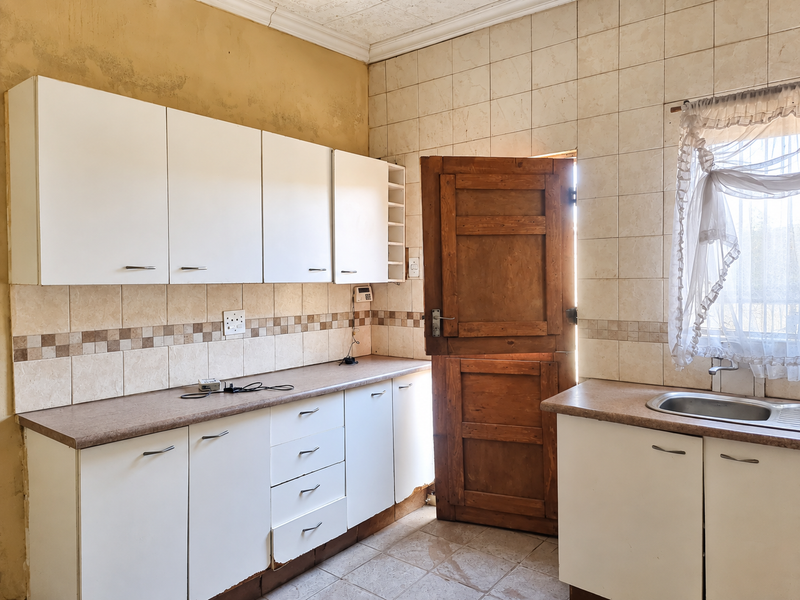 A dated kitchen featuring white cabinetry, tiled backsplash, and a stainless steel sink, requiring cosmetic updates to modernize the space.