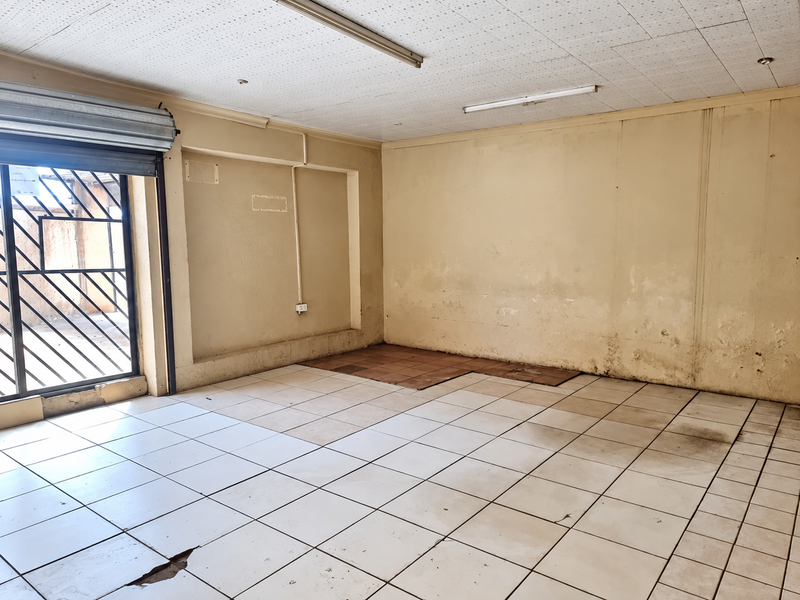 An empty garage space featuring tiled flooring, a roller shutter door, and security gate, requiring maintenance and cosmetic updates to improve its condition.