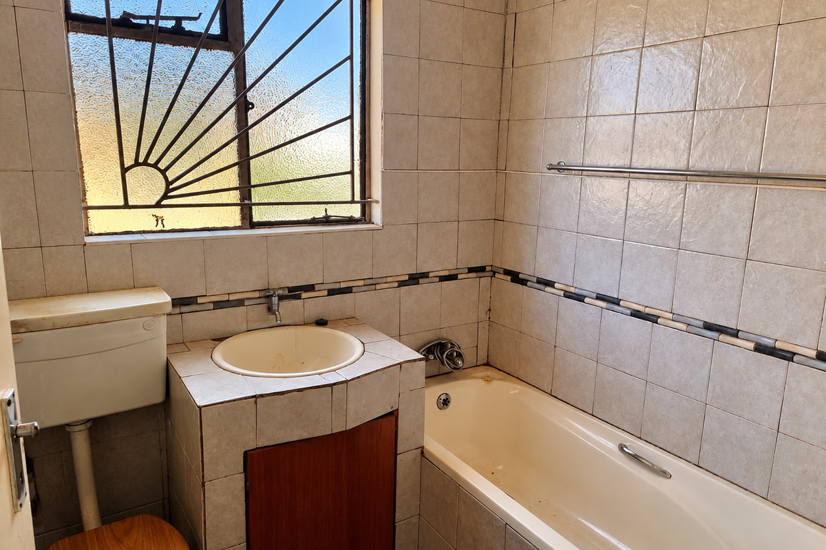 A dated bathroom featuring a built-in vanity with drop-in sink, a standard bathtub, and tiled walls with decorative border accents.