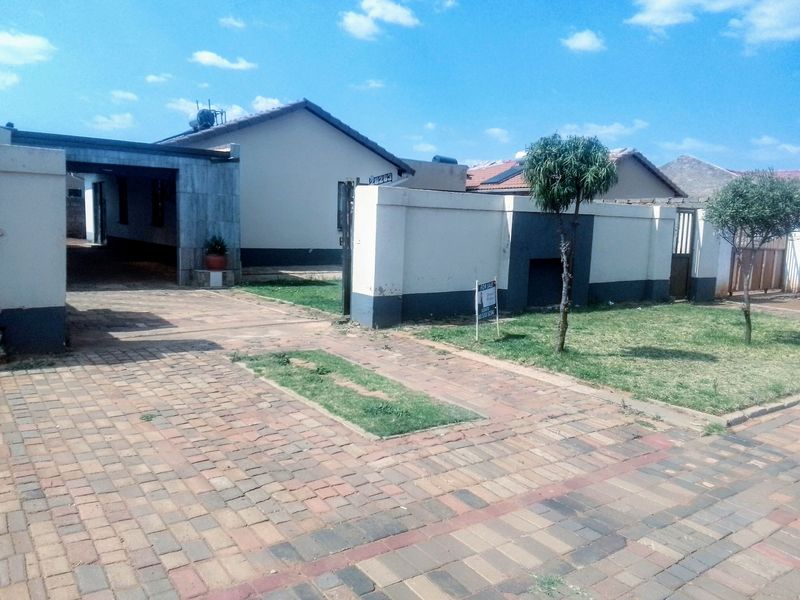 Front exterior view of the property featuring a paved driveway, carport, and boundary wall with solar water heating infrastructure.