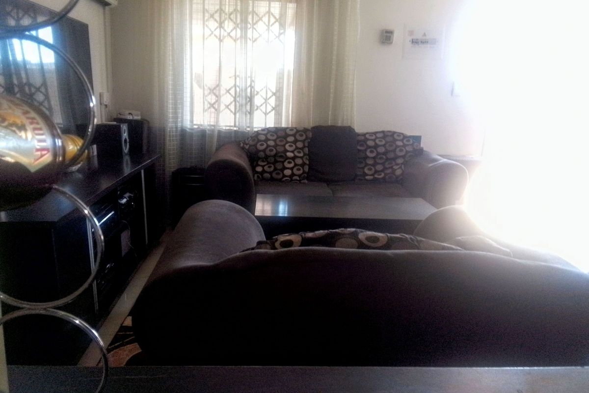 A living room area featuring a window with a security gate and a wall-mounted air conditioning unit.