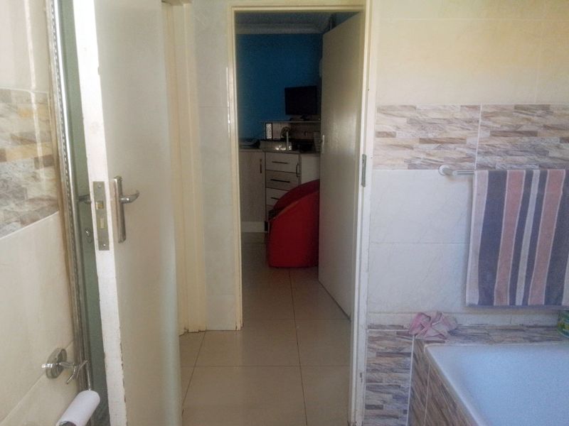 A bathroom featuring tiled walls and flooring with a built-in bathtub, providing access to an adjacent room.