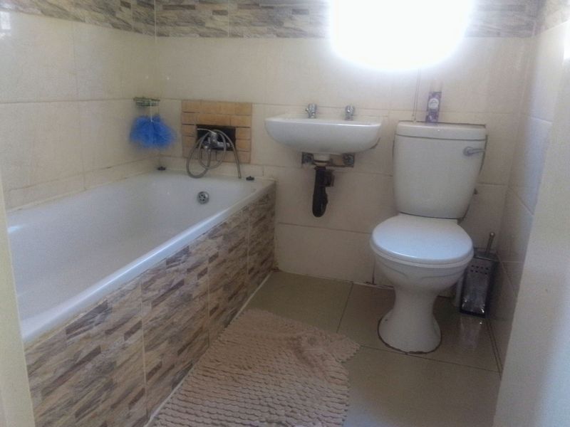 A functional bathroom featuring a bathtub, wall-mounted basin, and toilet with tiled finishes throughout.