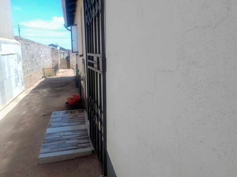 A side exterior view of the property featuring a security gate, tiled entrance step, and a concrete pathway along the boundary wall.