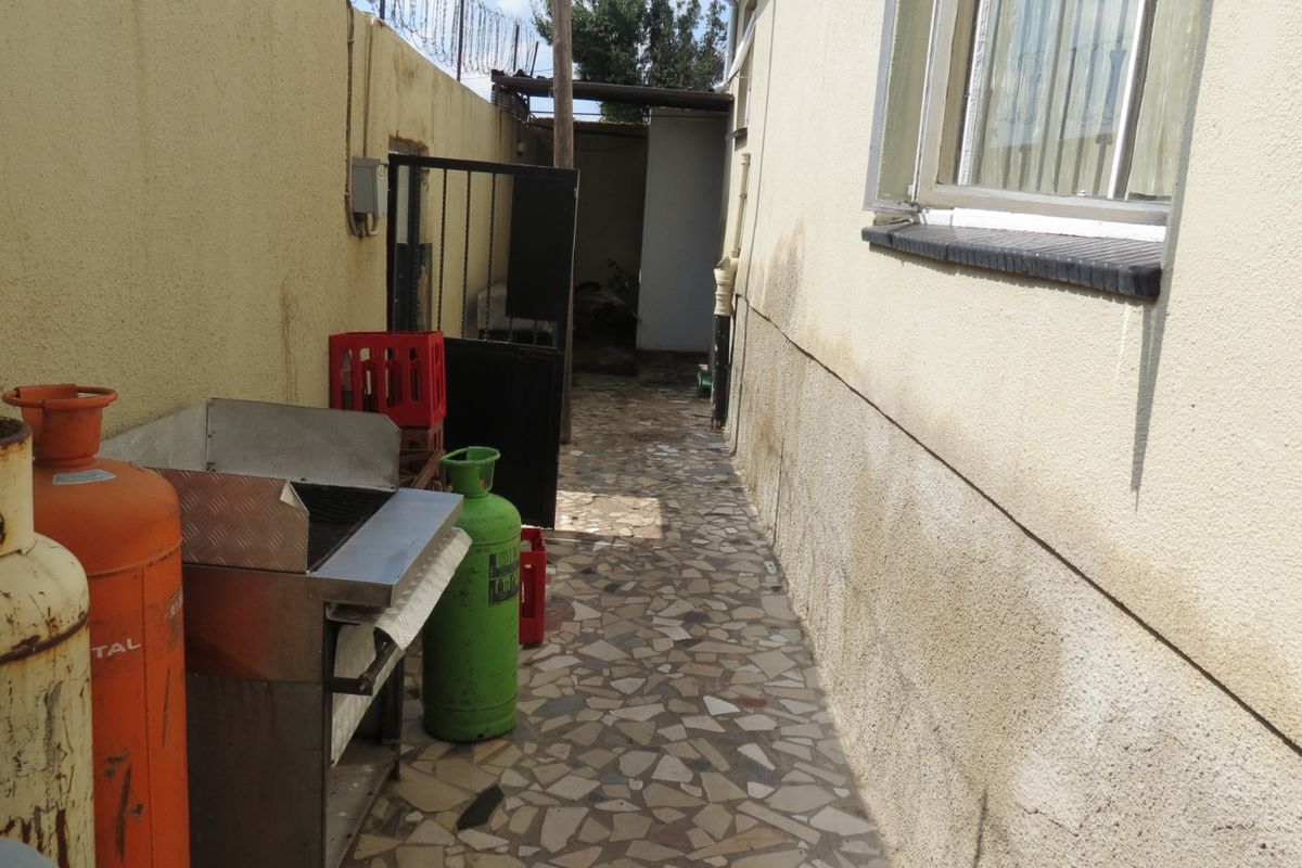 A narrow rear exterior walkway featuring paved flooring and an external wall showing signs of damp and weathering.