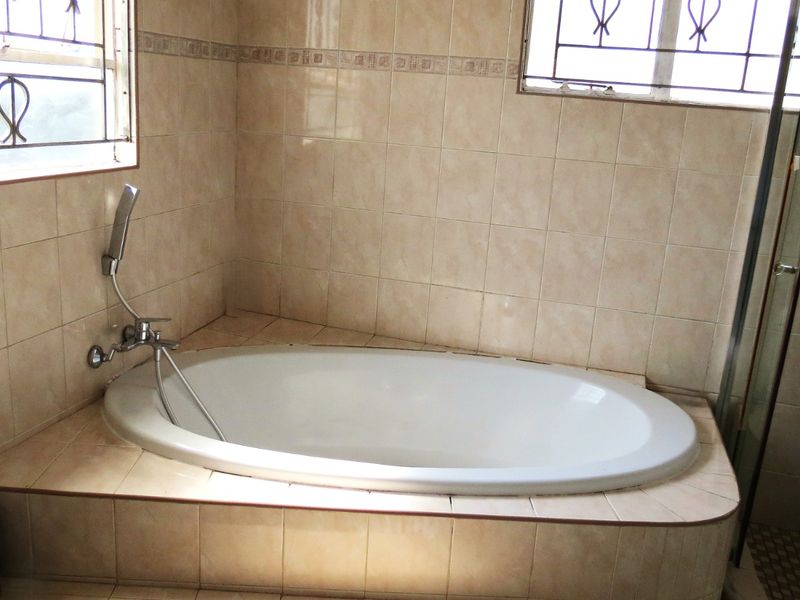 A functional bathroom featuring a built-in bathtub with a handheld shower mixer, tiled surround, and security bars on the windows.
