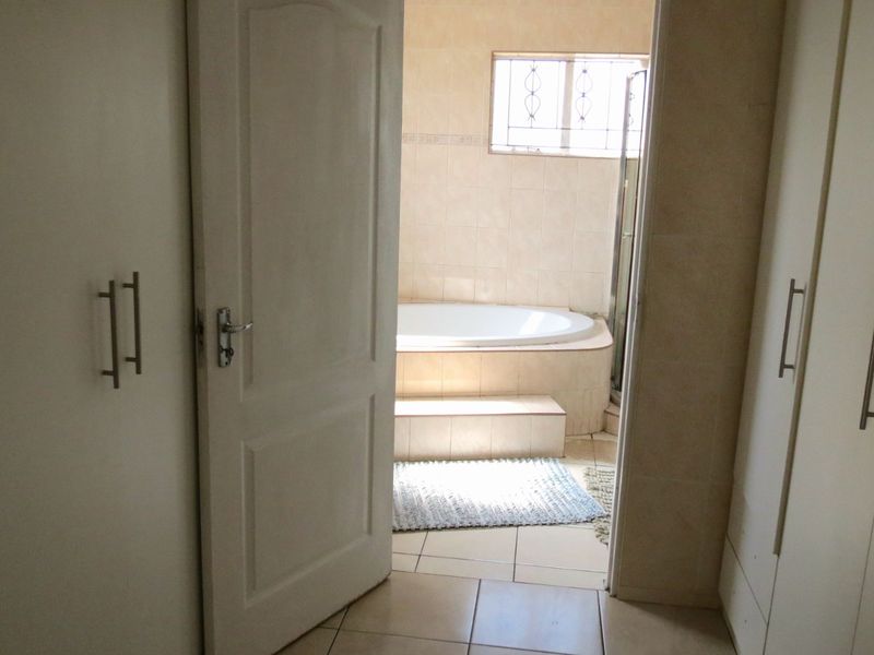A bathroom featuring a built-in bathtub with tiled surround, accessed through a dressing area with ample built-in cupboard storage.