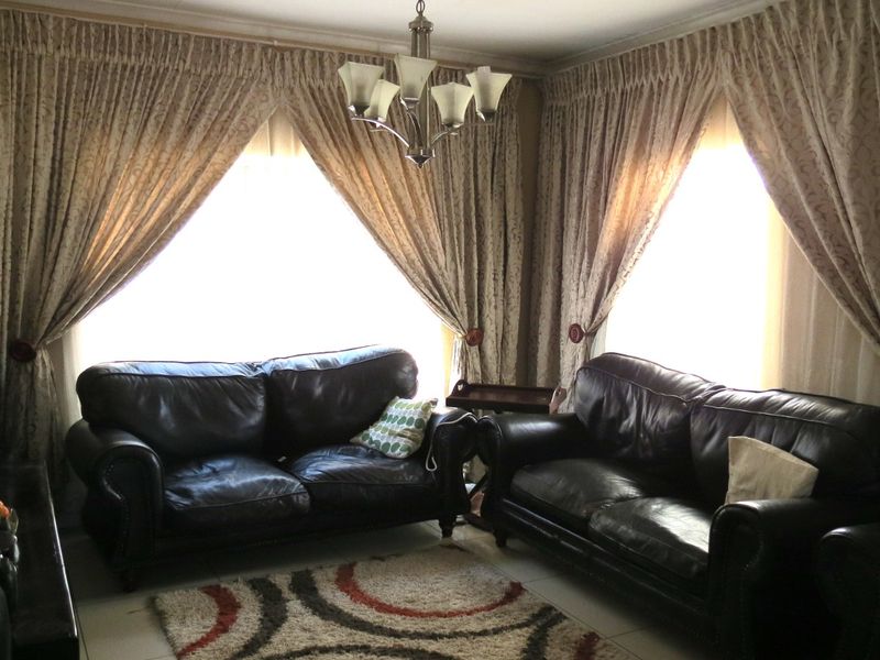 A comfortable living room featuring tiled flooring, a central ceiling light fixture, and large windows dressed with floor-to-ceiling curtains.