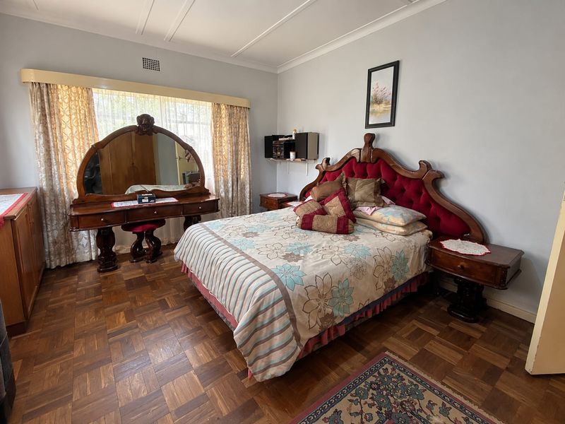 A spacious bedroom featuring classic parquet flooring, neutral wall finishes, and a large window with integrated curtain pelmet.