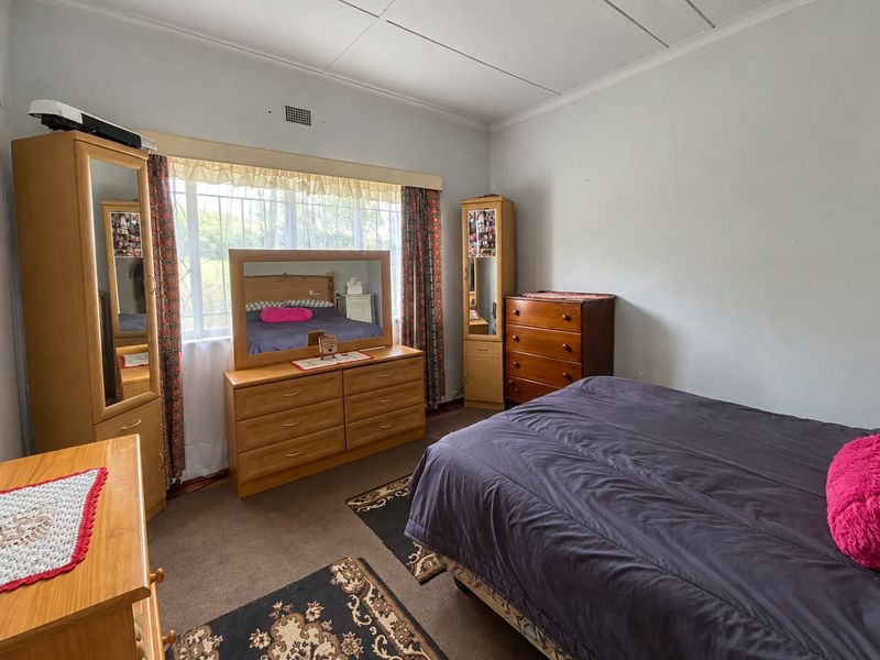 A bedroom featuring a large window with security bars and a ceiling vent, currently finished with carpet flooring and neutral wall paint.