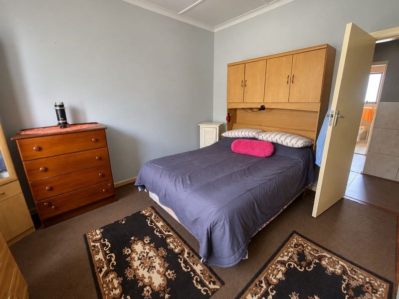A functional bedroom featuring built-in wooden cupboards, carpeted flooring, and neutral wall finishes, offering a practical layout for a comfortable sleeping space.